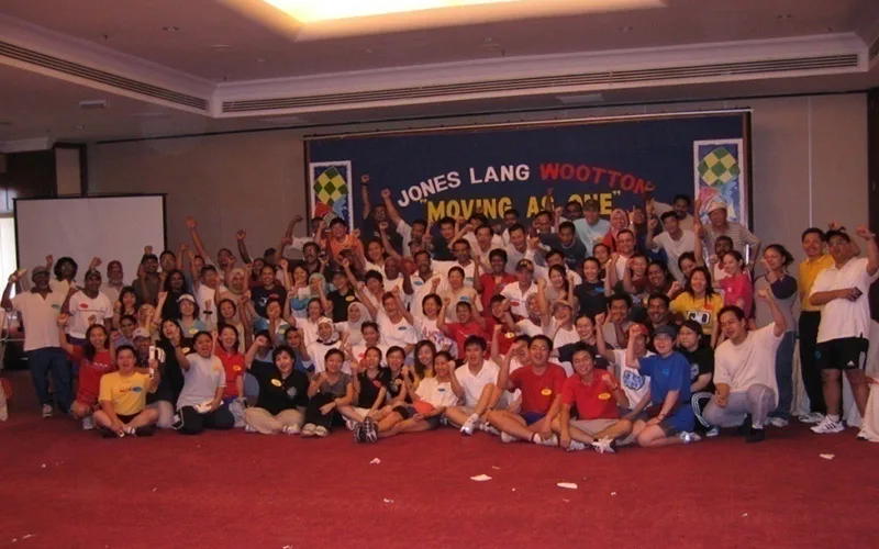 A ballroom full of Jones Lang Wootton staff cheering under their Moving As One banner