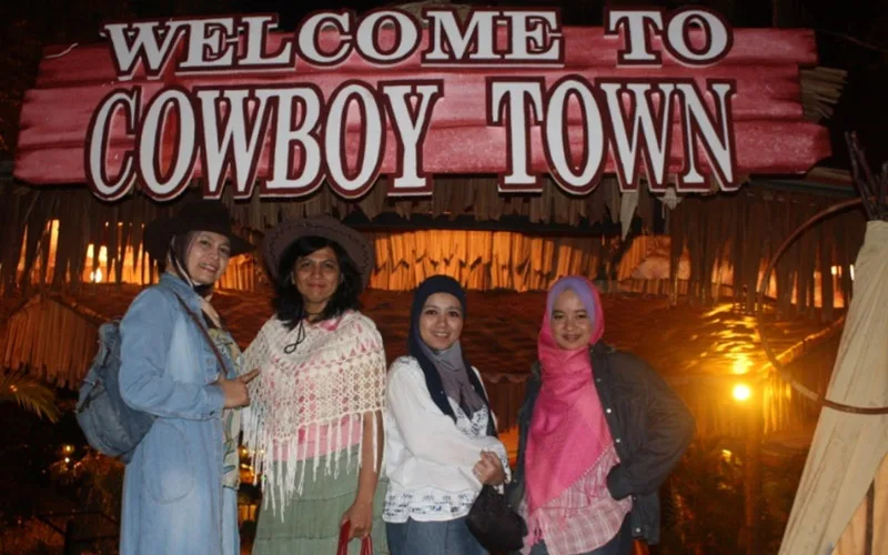 Four AKPK participants in cowboy-themed outfits at the Cowboy Town entrance at night