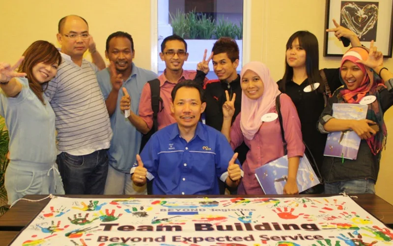 Beyond Logistics participants behind a handprint banner reading Team Building Beyond Expected Service