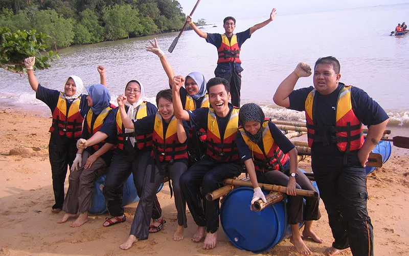 Maybank participants in life jackets celebrating beside their home-made barrel raft on the beach