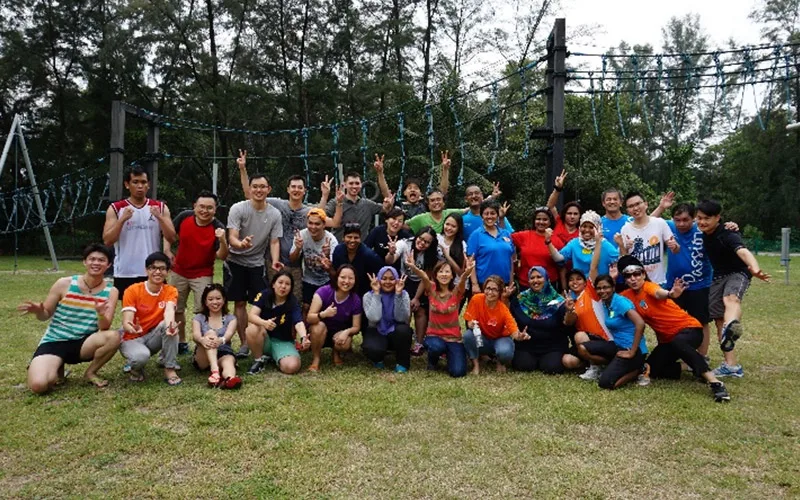 A group cheering on the grass in front of a high rope course