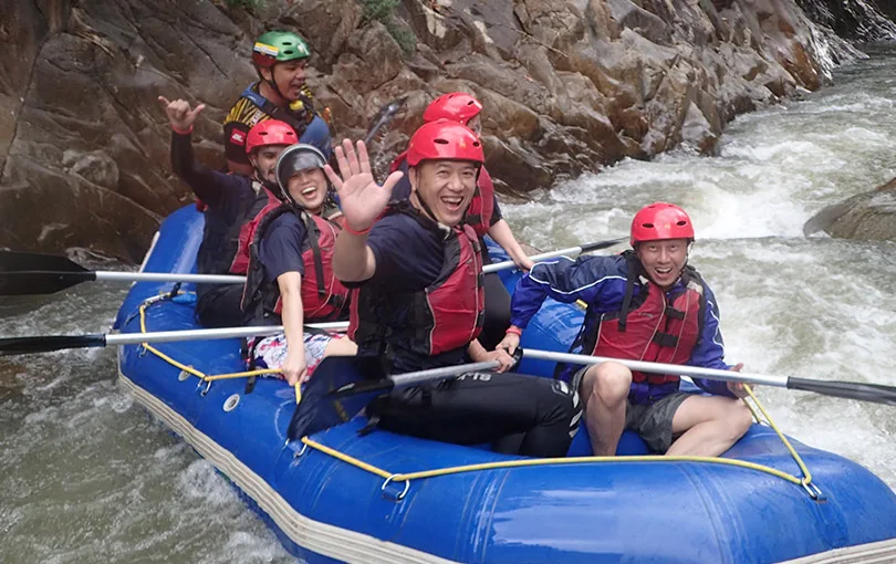 A team paddling a raft down river during a QOM outdoor programme
