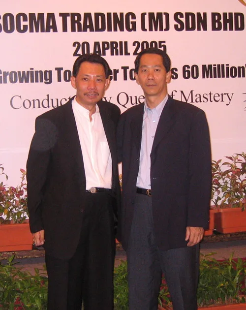 Two men in suits in front of a SOCMA Trading banner dated 20 April 2005, conducted by Quest of Mastery